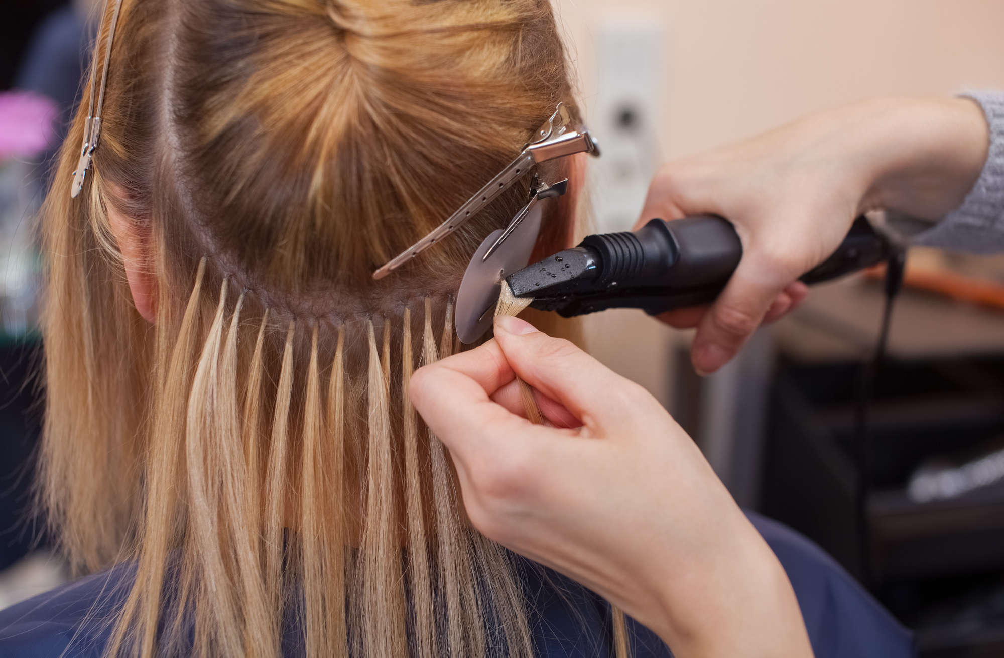 The hairdresser does hair extensions to a young girl, a blonde in a beauty salon. Professional hair care.